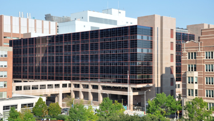 Exterior view of modern medical facility with large dark-windowed building, parking area, and surrounding urban architecture
