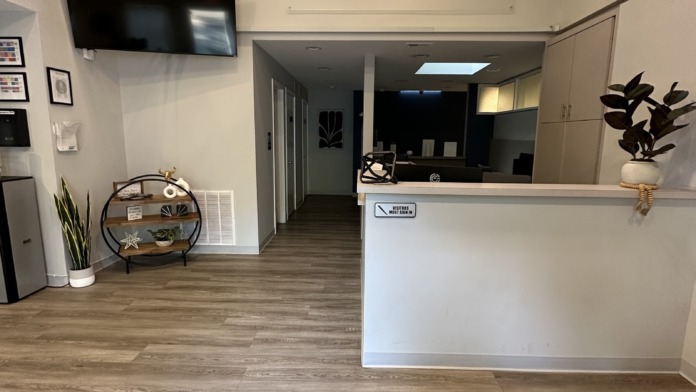 Interior reception area with welcome signage, white desk, TV screen, open floor plan, and modern facility finishes