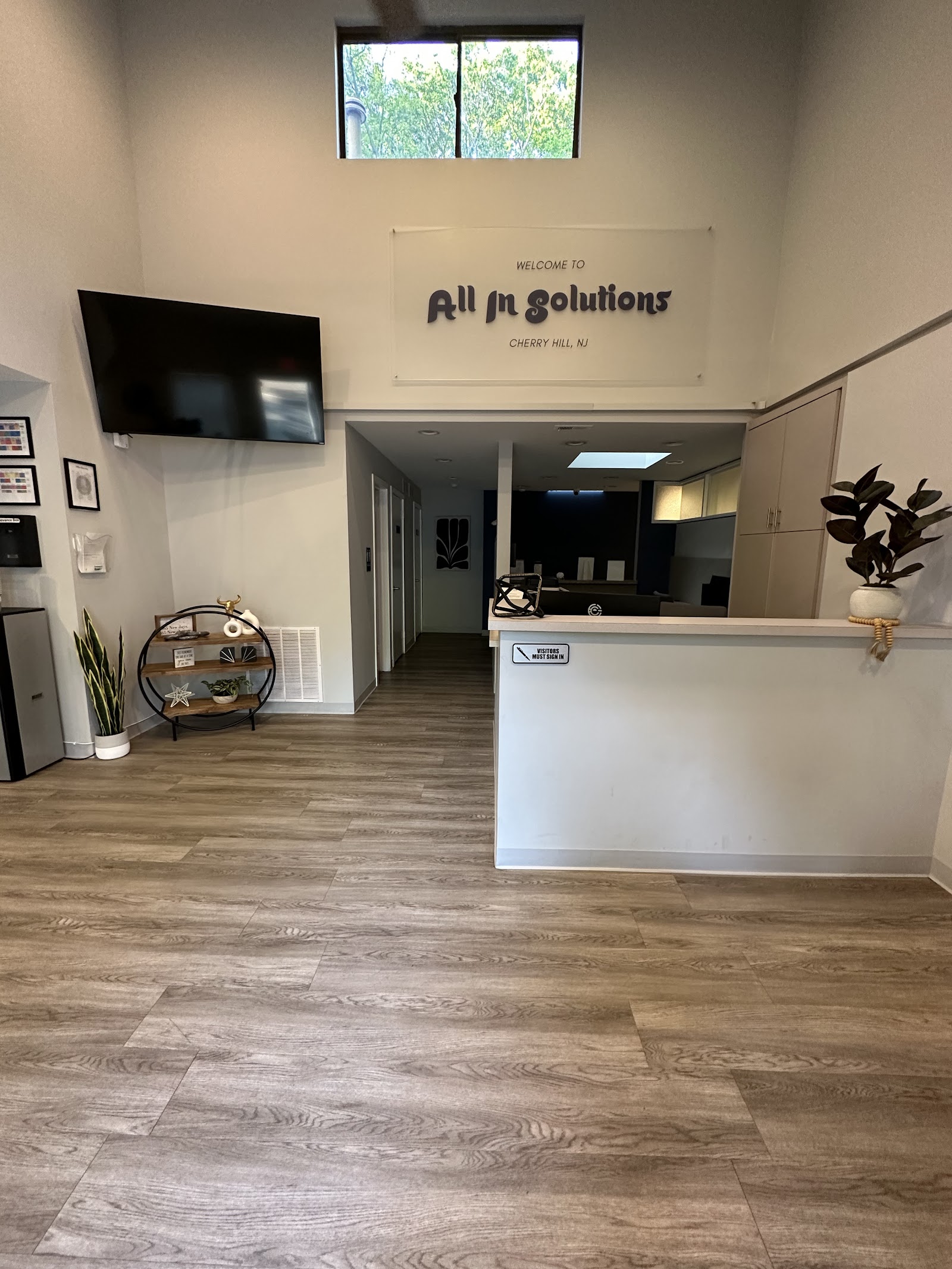 Interior reception area with welcome signage, white desk, TV screen, open floor plan, and modern facility finishes