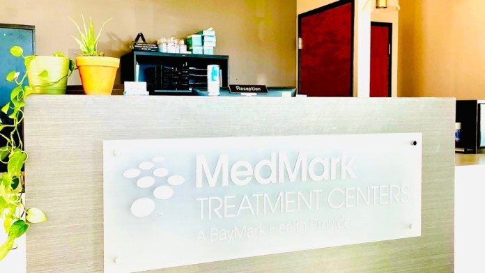 Interior lobby reception counter featuring MedMark Treatment Centers logo, pendant lights, front desk area with plants and modern furnishings