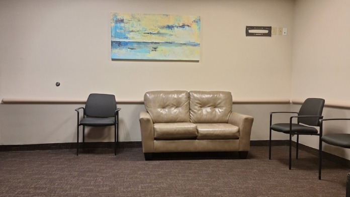 Interior waiting lounge with tan leather sofa, black chairs, recessed lighting, and abstract artwork on walls.