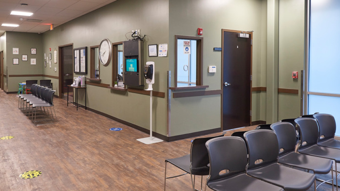 Interior large open reception area with reception desk, multiple seating zones, wood flooring, and numbered treatment room doors
