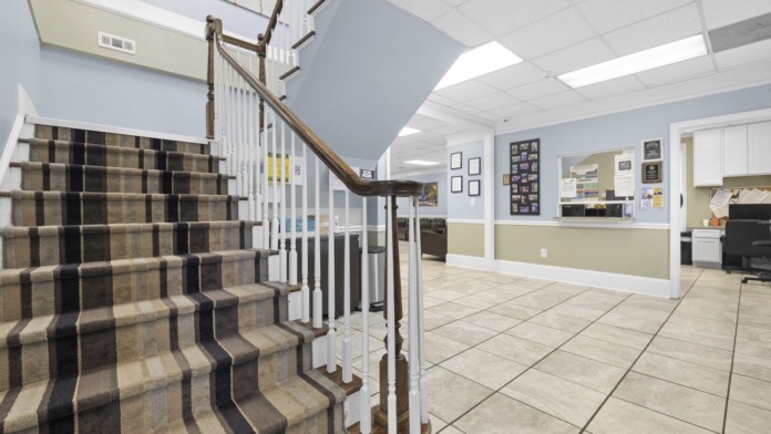 Interior showing carpeted staircase with white railings and reception area with light blue walls and windows