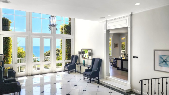 Interior entry foyer with marble floors, dual staircases, large ocean-view windows, and modern chandelier lighting