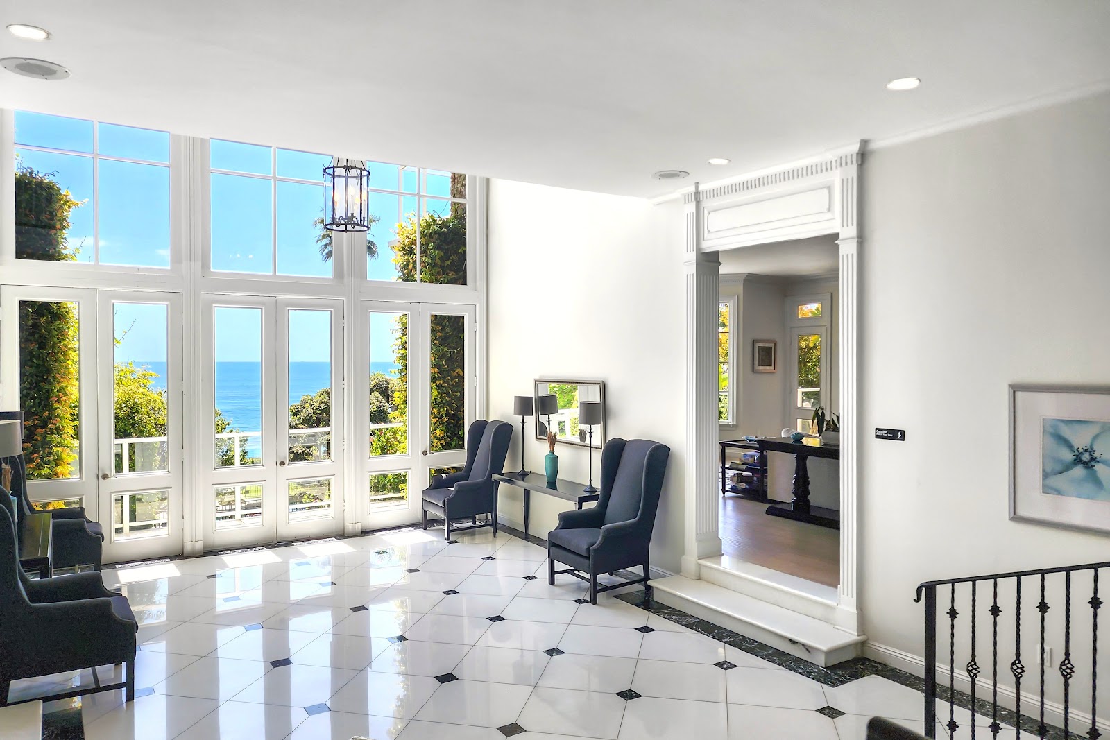 Interior entry foyer with marble floors, dual staircases, large ocean-view windows, and modern chandelier lighting