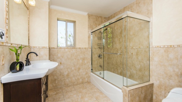 Interior bathroom with beige tile, dark wood vanity, glass-enclosed shower surround and window light