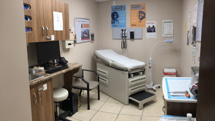 Interior medical examination room with exam table, computer workstation, cabinetry, and health education posters on walls