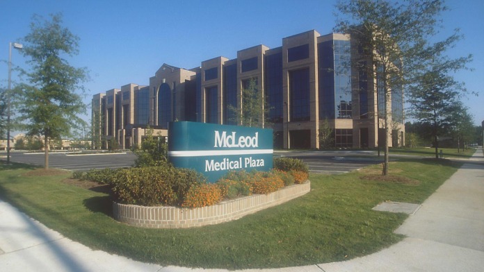 Modern medical plaza building showing vertical architectural elements and blue McLeod Medical Plaza signage with landscaping