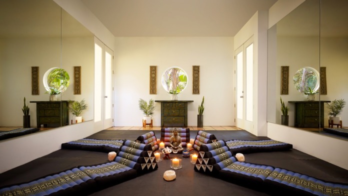 Interior meditation space with floor cushions, candles, Buddha statue, and decorative wall panels
