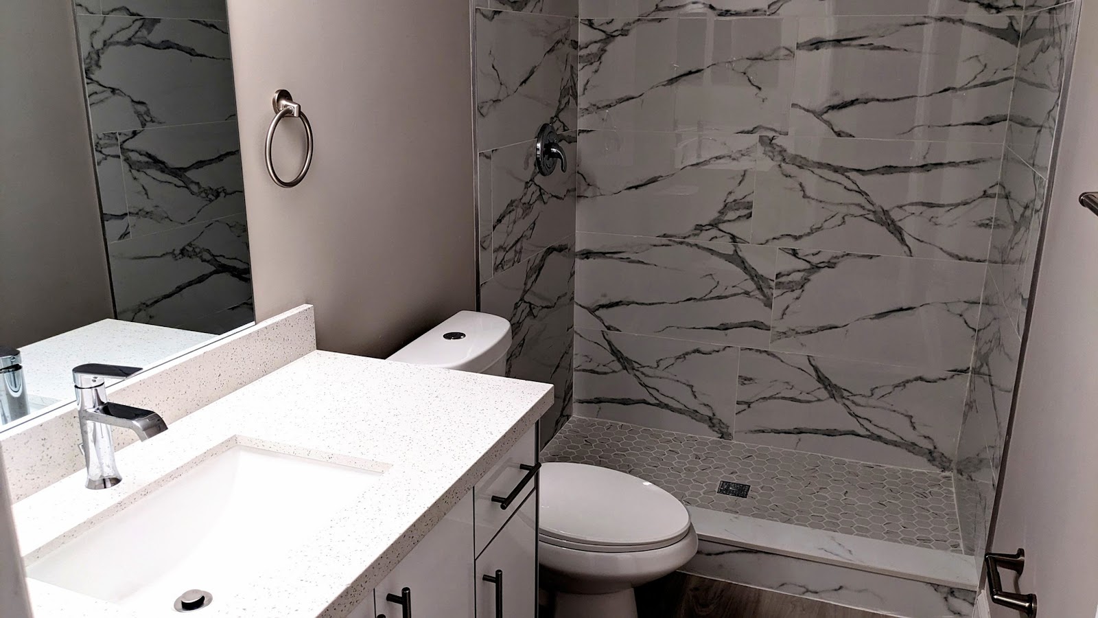 Interior bathroom with white vanity, marble-patterned tile walls, walk-in shower with glass enclosure, and toilet