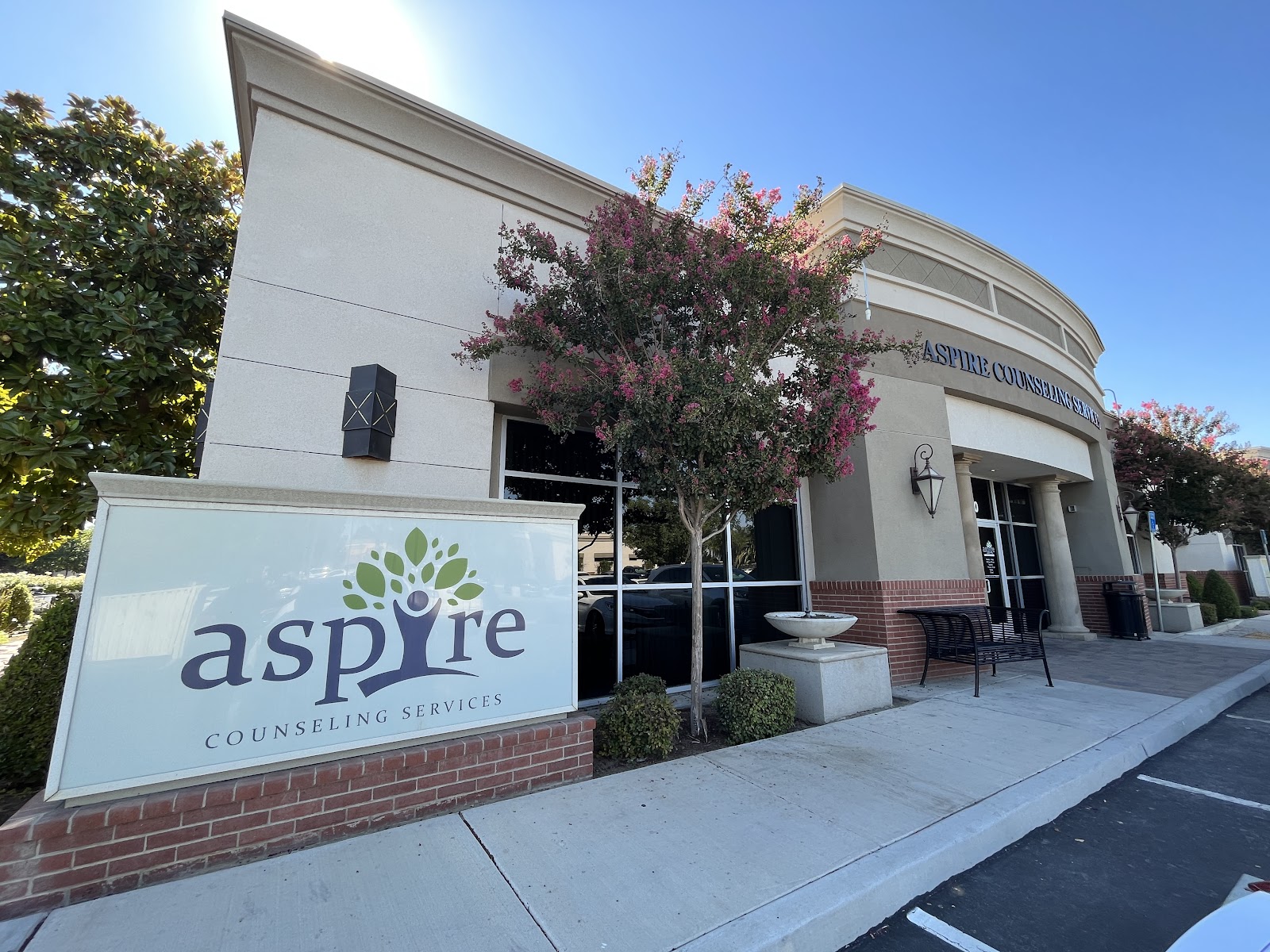 Exterior angle of facility showing white stucco walls, brick base, rounded architecture, and flowering plants