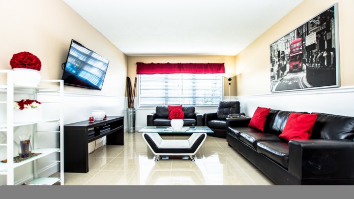 Interior common area with black leather seating, red accent pillows, white display shelving, flat-screen TV, and contemporary furnishings