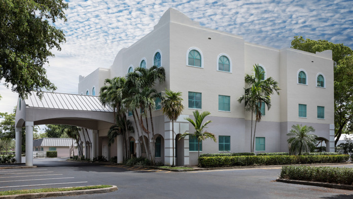 Exterior front entrance with modern white building, palm trees, porte cochere canopy, and circular driveway
