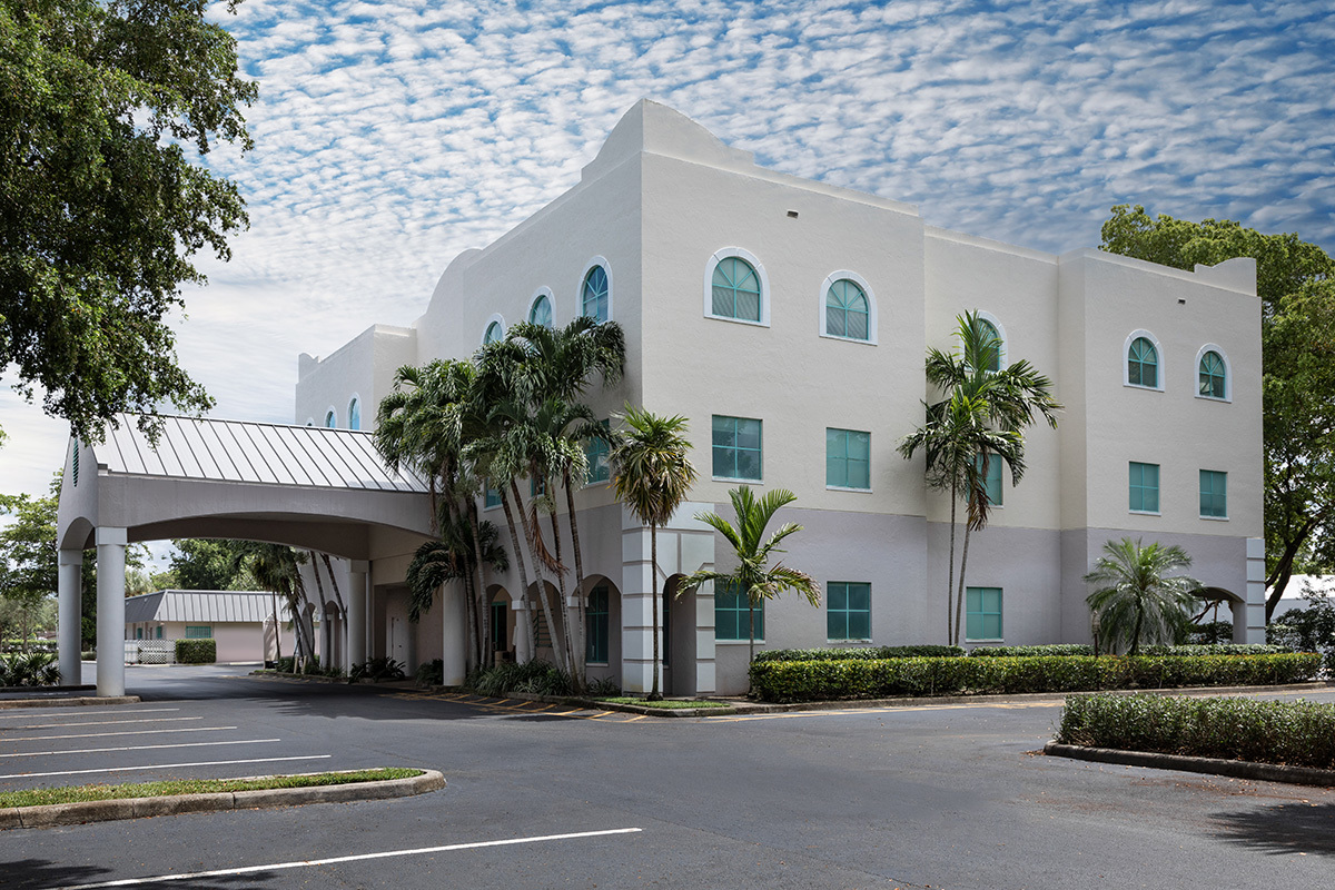 Exterior front entrance with modern white building, palm trees, porte cochere canopy, and circular driveway