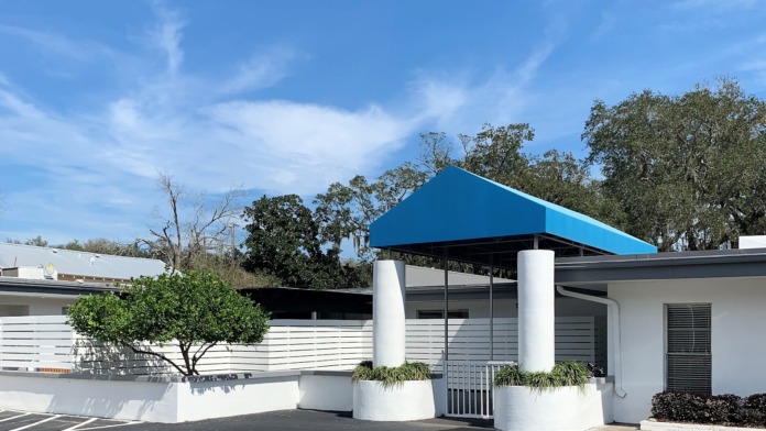 Exterior front entrance of treatment center featuring white modern architecture, blue covered entry area, and landscaped grounds