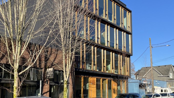 Exterior of modern treatment facility showing dark metal cladding building facade with large window panels and parked vehicles on city street.