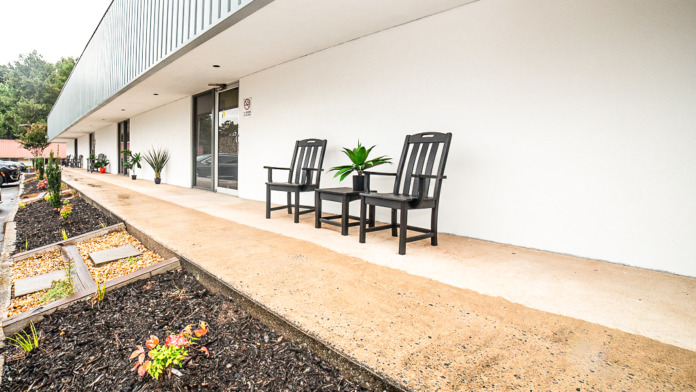 Exterior covered patio with black adirondack chairs, landscaped garden beds, and contemporary building architecture with clean lines