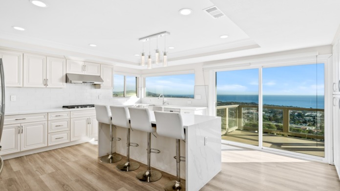 Interior gourmet kitchen with white cabinetry, marble countertops, bar seating, and ocean views