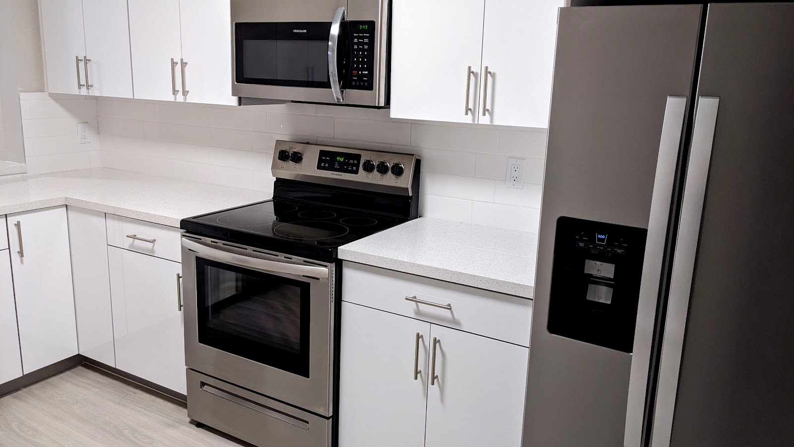 Interior kitchen featuring white cabinetry, stainless steel range and refrigerator, microwave, and white countertops