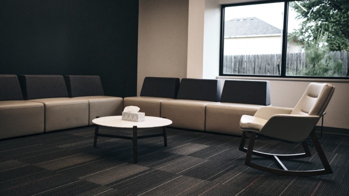 Interior lounge space with beige and gray modular seating, white side table, and windows overlooking outdoor grounds