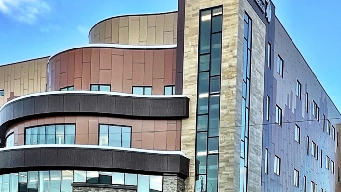Exterior view of modern multi-story treatment facility with curved stone and metal facade, large windows, and entrance signage