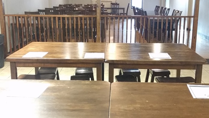 Interior space with wooden railing dividing levels, dining tables, chairs, and overhead lighting fixtures