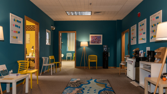 Interior space with teal walls, yellow and white striped modern chairs, yellow doors, patterned rug, decorative wall art, natural lighting from windows