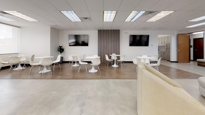 Interior common area with white dining tables, chairs, wall-mounted televisions, and modern lighting fixtures