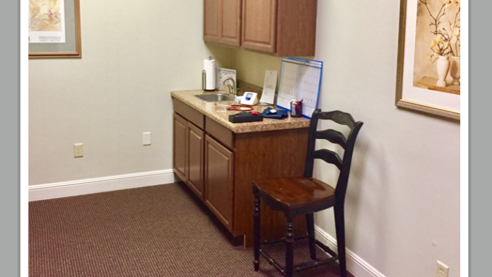 Interior nurses station with wooden desk, office chair, wall cabinets, framed art, and administrative workspace