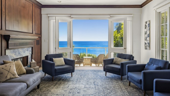 Interior living room with ocean views, fireplace, blue armchairs, and glass doors opening to terrace