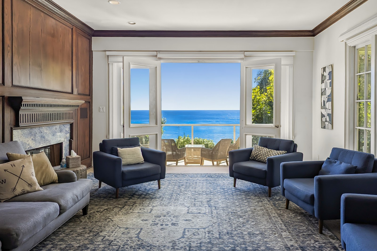 Interior living room with ocean views, fireplace, blue armchairs, and glass doors opening to terrace