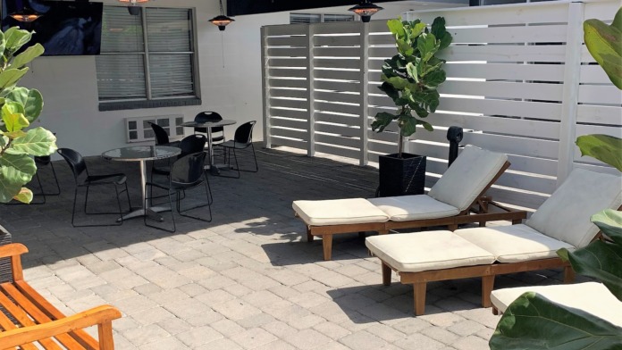 Exterior patio space with lounge chairs, dining tables, heat lamps, and white privacy screens overlooking waterfront