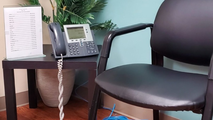 Interior office area with turquoise walls, desk with telephone and plant, black chair, and courtesy phone sign on wall