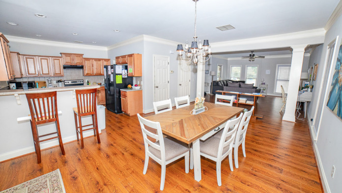 Interior multipurpose space with wooden dining table, kitchen area with wood cabinetry, and adjoining living room with furniture