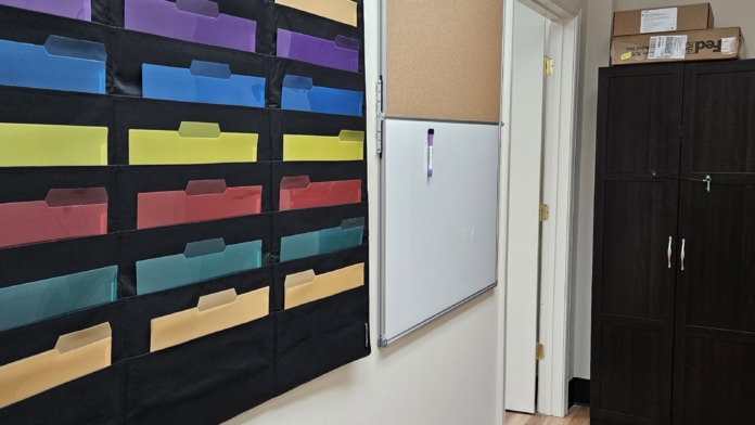Interior office space showing colorful wall-mounted organizational storage bins with rainbow dividers and white cabinets.