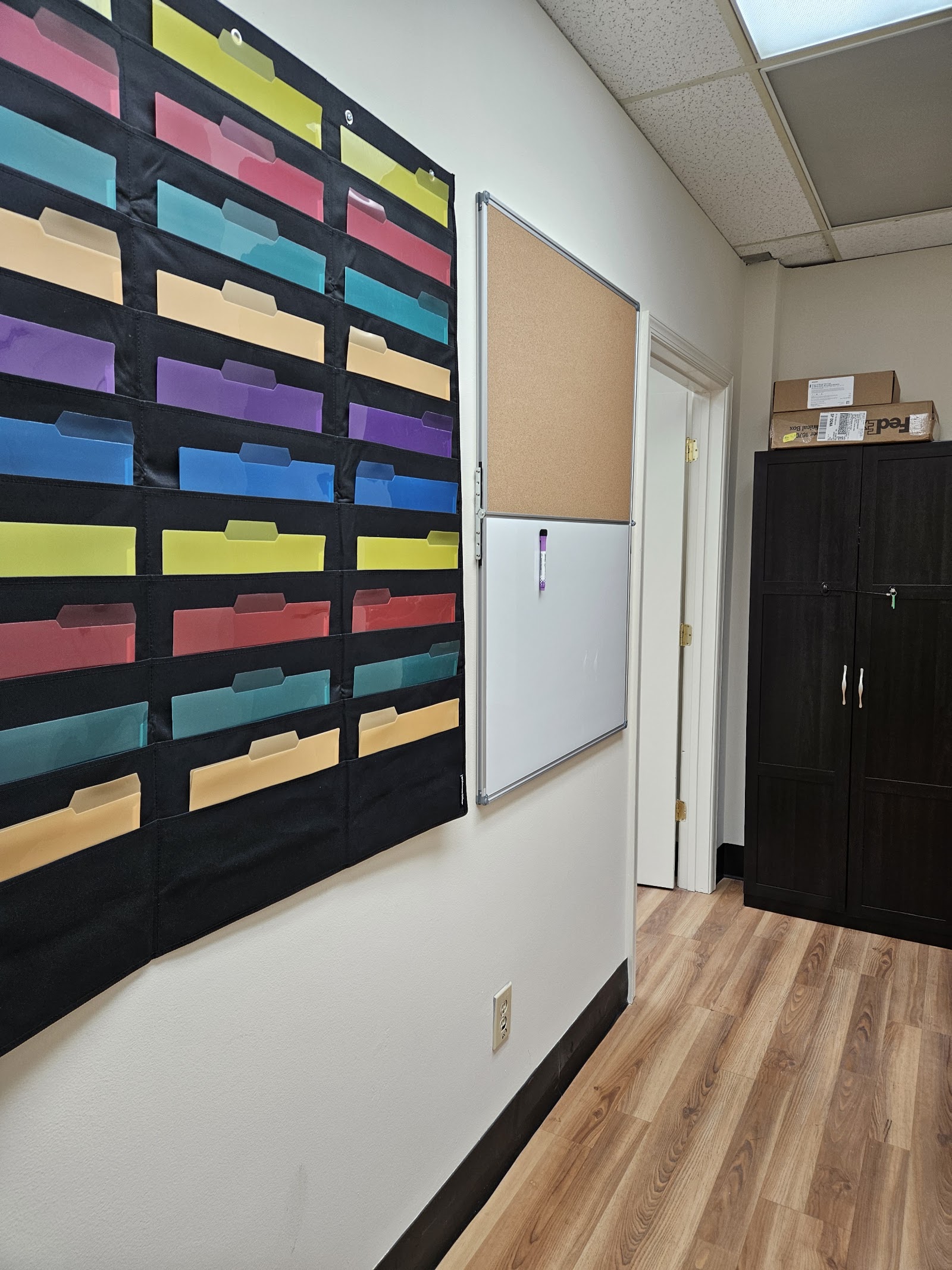 Interior office space showing colorful wall-mounted organizational storage bins with rainbow dividers and white cabinets.