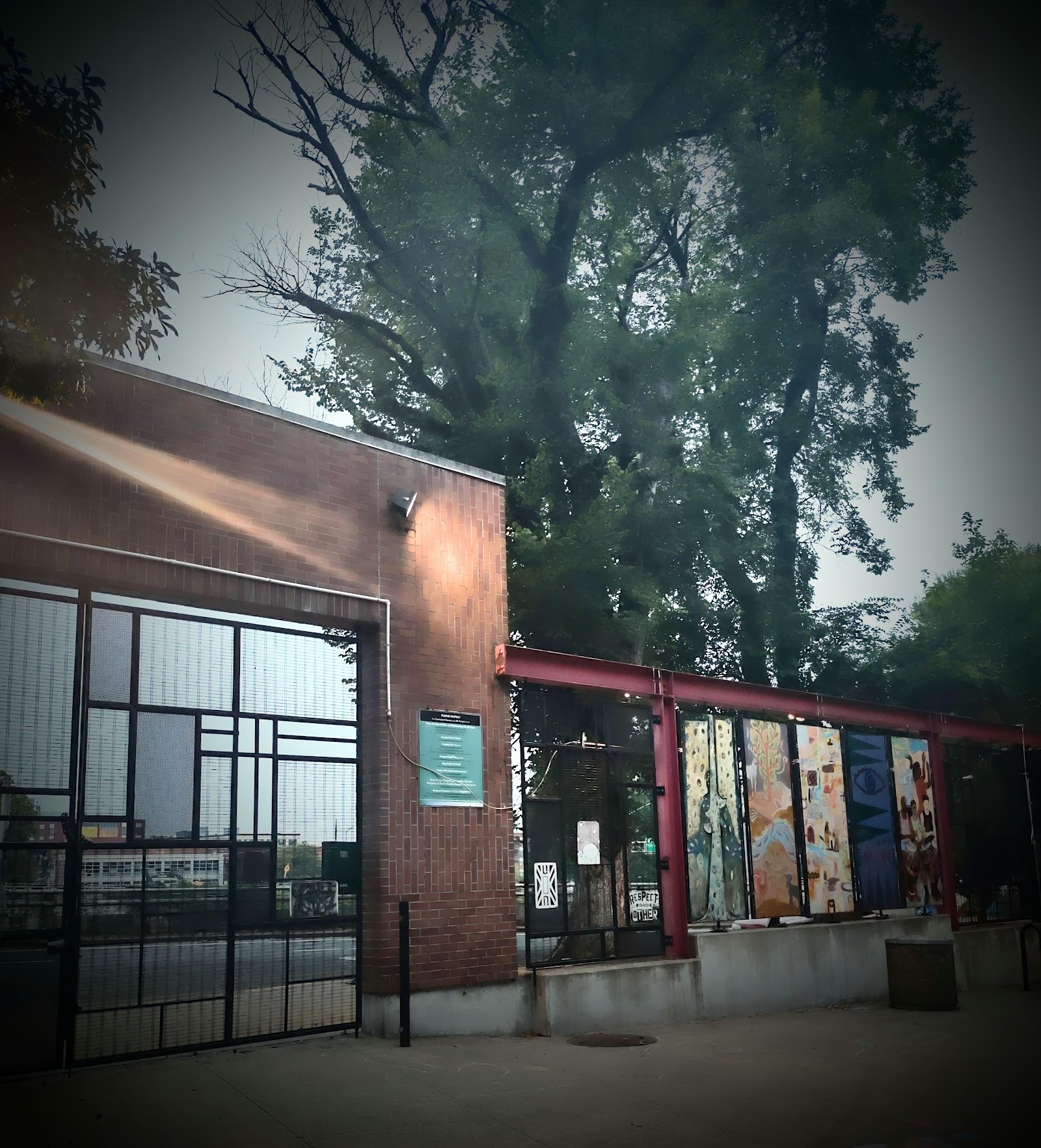 Outdoor gallery display with colorful art panels mounted on red metal frame structure under trees