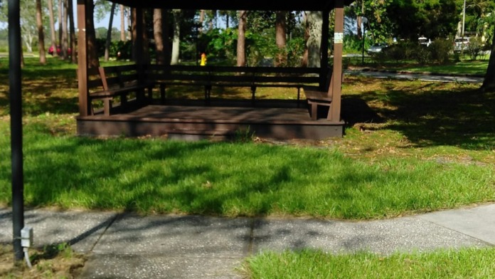 Outdoor covered gazebo shelter with seating surrounded by mature trees and manicured grass areas