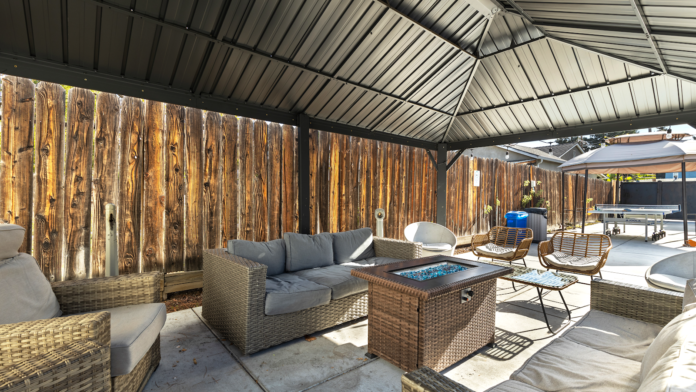 Exterior patio with wicker seating, decorative wooden wall, fire pit table, and covered shade structure