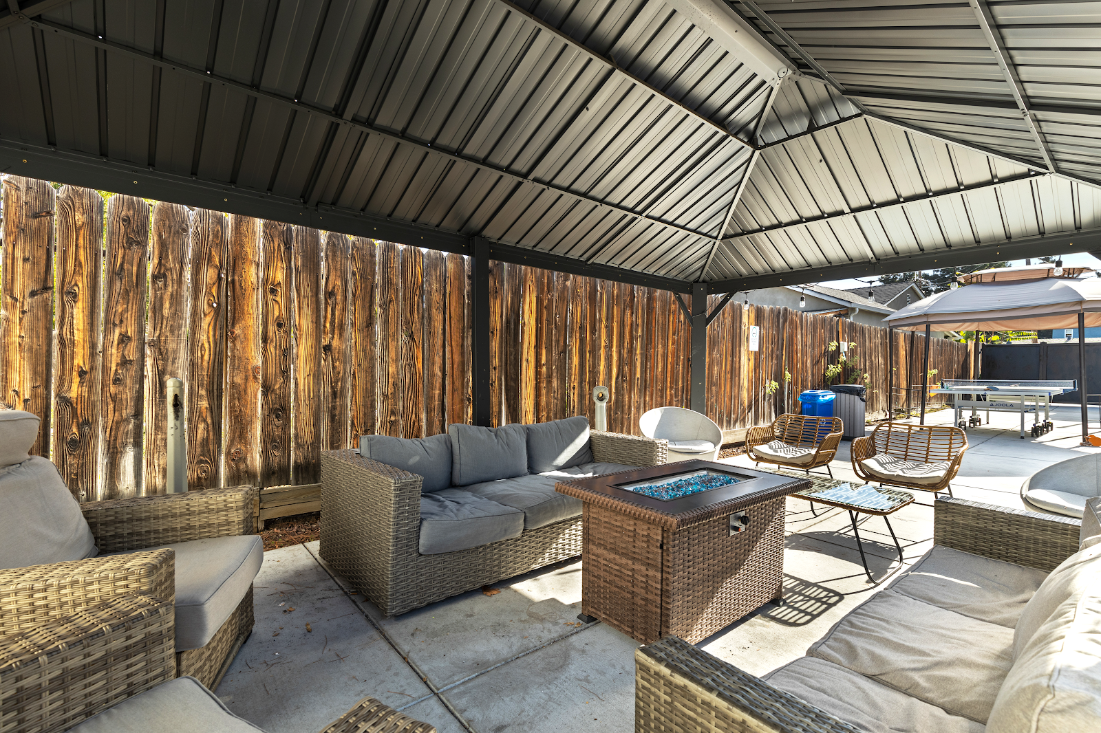 Exterior patio with wicker seating, decorative wooden wall, fire pit table, and covered shade structure