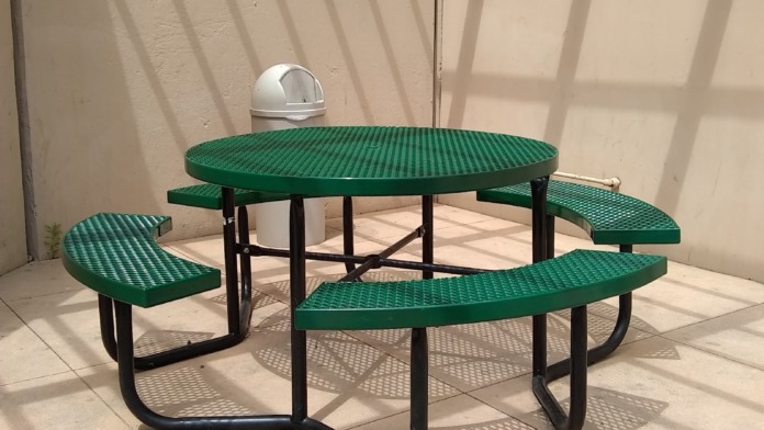 Outdoor patio space with green metal picnic table and benches, concrete floor, beige walls, and skylight overhead