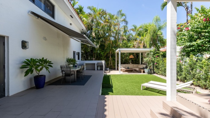 Exterior patio space with seating areas, manicured lawn, palm trees, and covered pergola structures