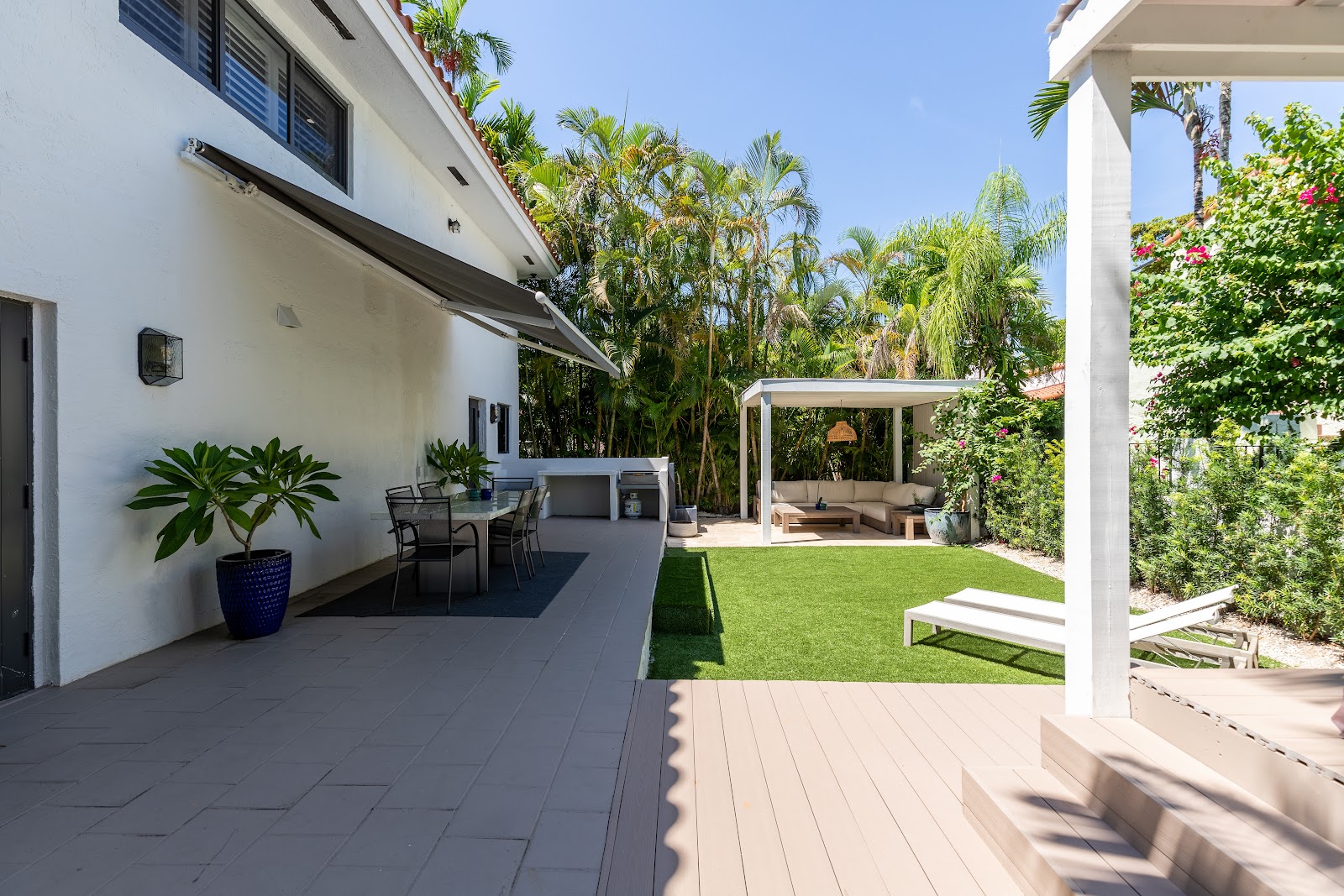 Exterior patio space with seating areas, manicured lawn, palm trees, and covered pergola structures