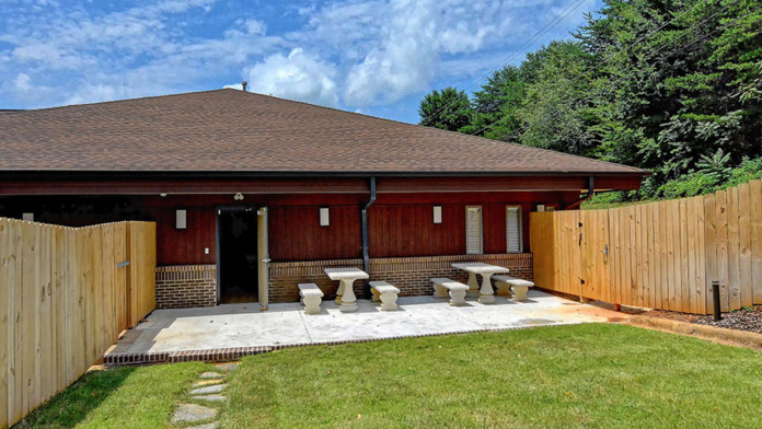 Exterior patio with concrete seating platforms, green lawn, red building structure, and wooden privacy fence
