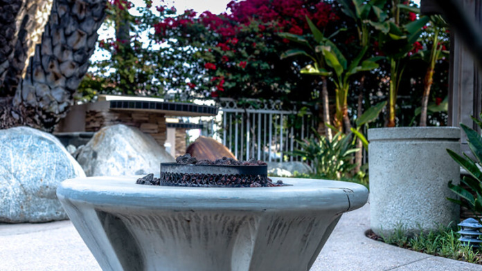Exterior patio area featuring fire pit, seating rocks, flowering plants, and wooden railings