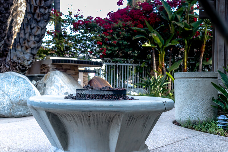 Exterior patio area featuring fire pit, seating rocks, flowering plants, and wooden railings