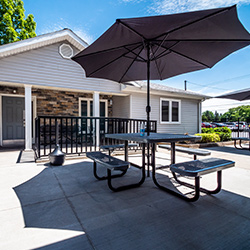 Outdoor patio area with picnic table and large black umbrella on concrete pad, facility building background