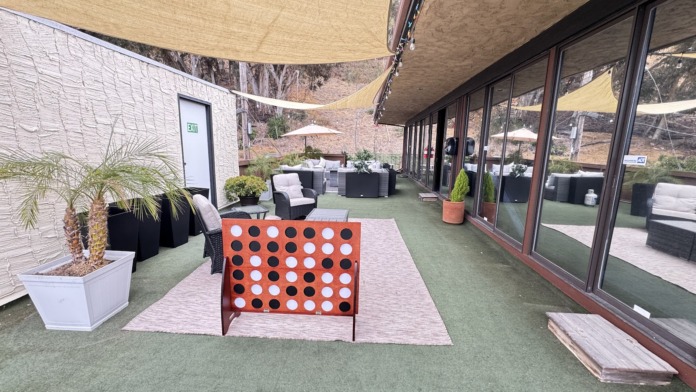Covered outdoor patio with artificial turf, shade sails, lounge furniture, plants, and glass entry doors.