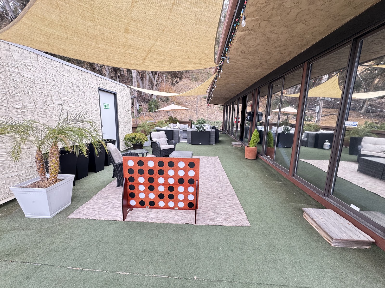 Covered outdoor patio with artificial turf, shade sails, lounge furniture, plants, and glass entry doors.