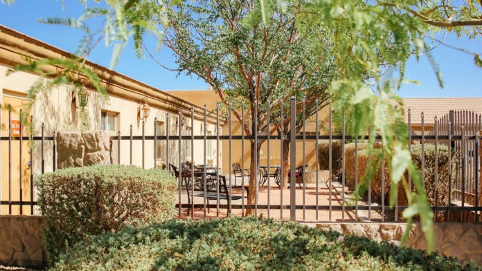 Exterior recreational area showing disc golf basket with yellow flag on desert landscape, trees in background, recreational amenity